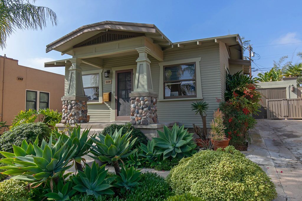 green Craftsman house with low maintenance garden in the front- long driveway leads to a garage