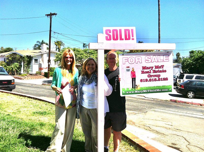 Realtor and Clients Standing on a Just Sold Sign