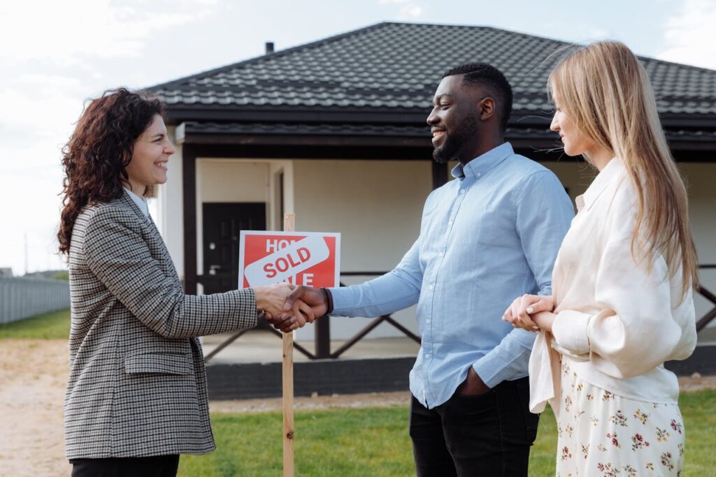 A Couple Shaking Hands with their Realtor with a Sold Sign on the Background
