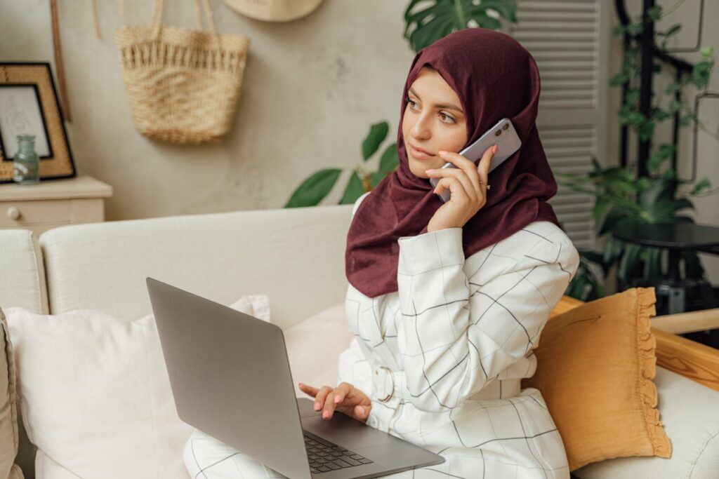 A Woman in a Hijab Using a Computer and Talking through the Phone