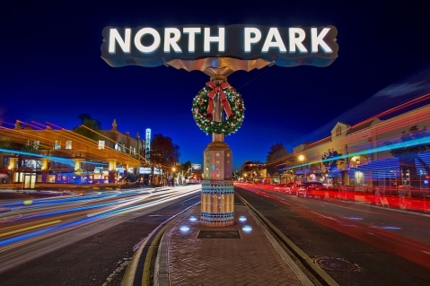 Illuminated North Park sign at night with a holiday wreath, featuring long-exposure light trails from traffic and the vibrant glow of University Avenue.